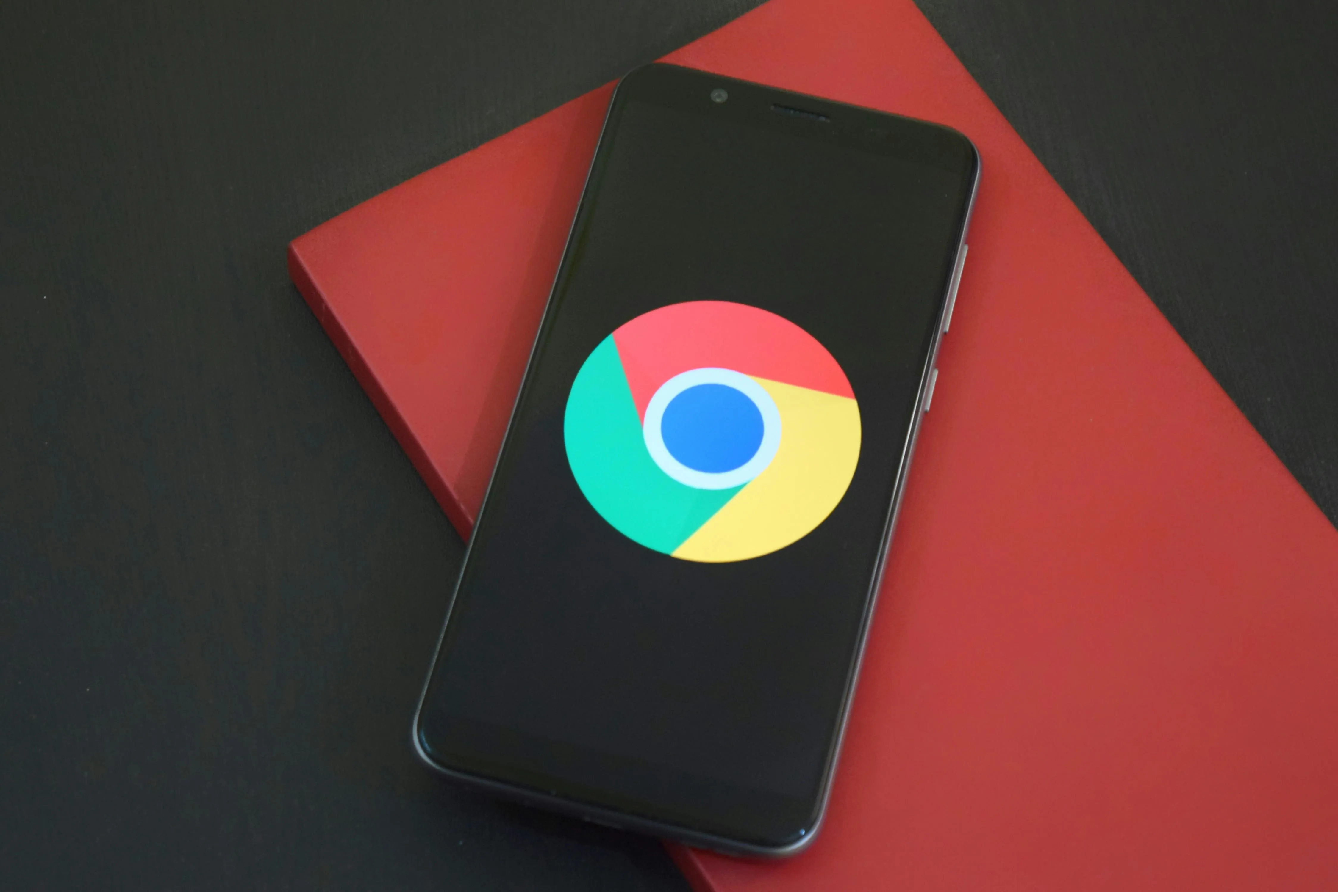 Free Close-up of a smartphone with Chrome browser logo on screen placed on a red notebook.