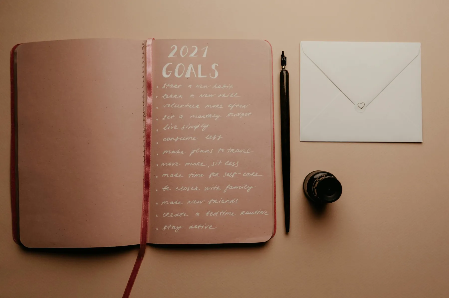 Free Open notebook with 2021 goals, calligraphy pen, envelope, and ink jar on neutral background.