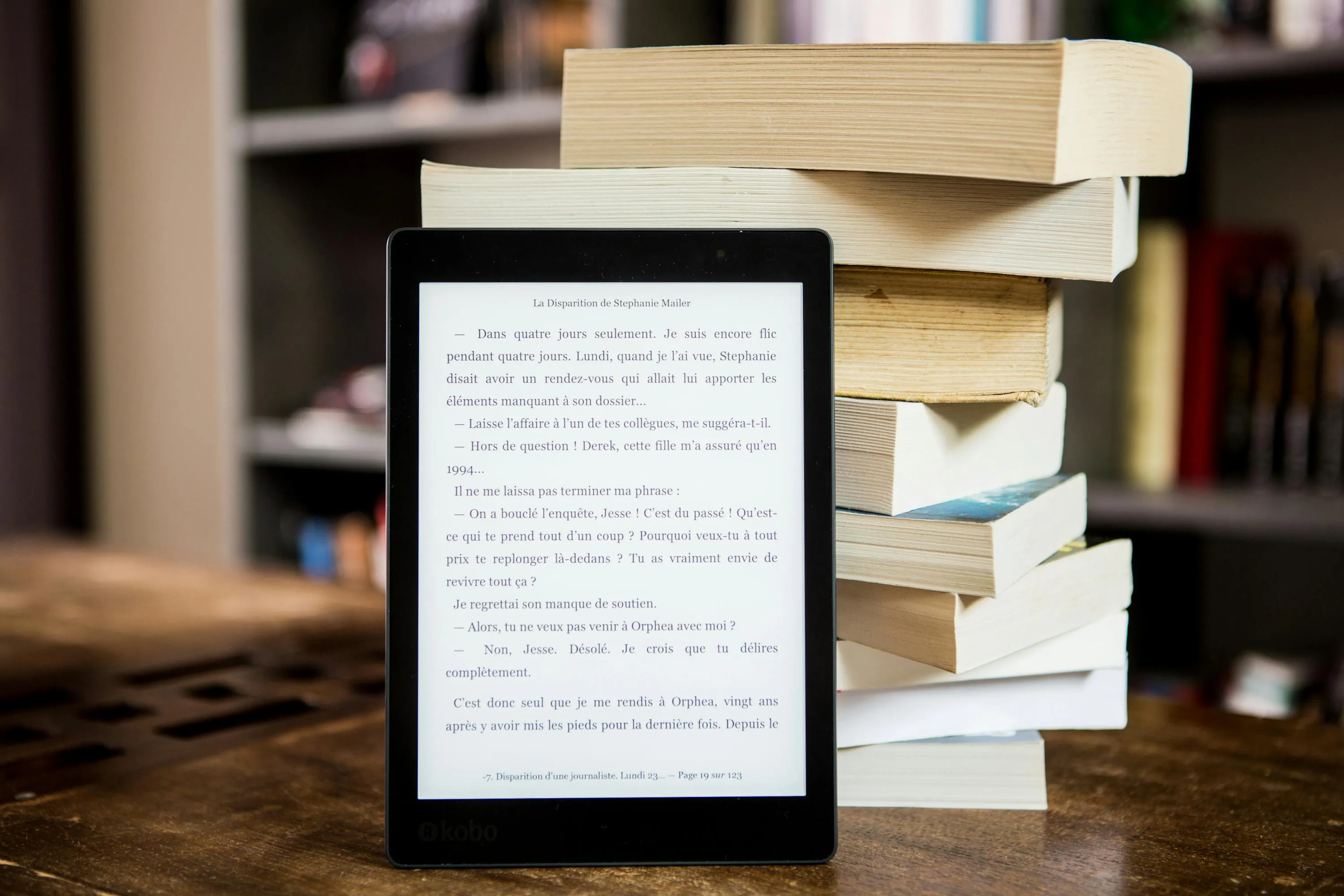 Free E-reader with text displayed next to a stack of physical books on a wooden table.
